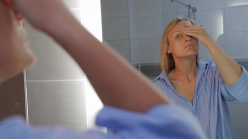 Woman Applies Facial Cream in Bathroom Mirror