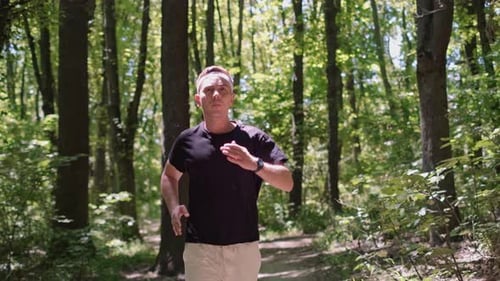 A portrait of a man in sportswear jogging in the forest. Running trails in forests and parks are equ