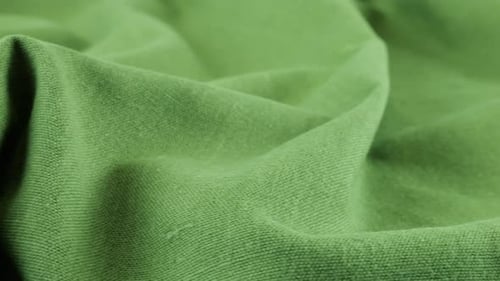 Close-up view of the soft folds of the pistachio green linen fabric. The textile background rotates