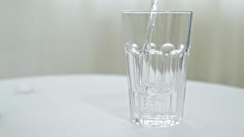 Pouring Water From Bottle Into Glass on White Background