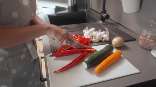 A woman is using a knife to slice a red bell pepper on a cutting board.