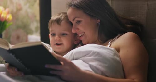 Woman and Child Reading Book in Bed