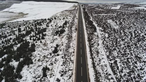 Long empty road aerial into distance across highland snowy countryside moors tilt down birdseye