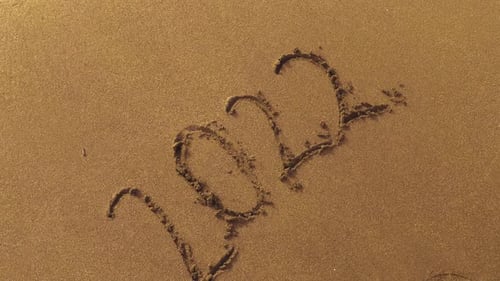 Sea wave washes away inscription 2022 on sand and disappears without trace.
