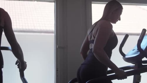 Women run on treadmill and elliptical at gym, slow-mo, pan
