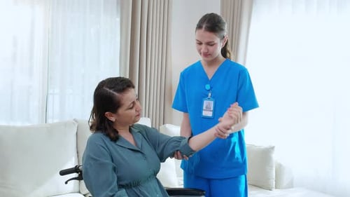 Young nurse therapy with patient while stretching muscle hand in living room at home.