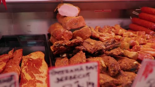 Meat department worker adding smoked chuncks of beef rib eye in shop window.