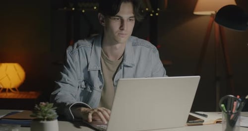 Young Man Working with Laptop Computer Sitting at Desk Concentrated on Work in Office at Night