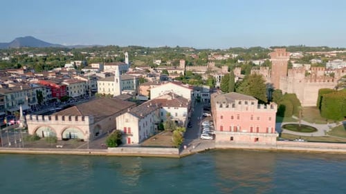 Les bâtiments anciens admirent le coucher de soleil en soirée alors que les touristes font la queue sur la promenade au bord du lac. Lazise