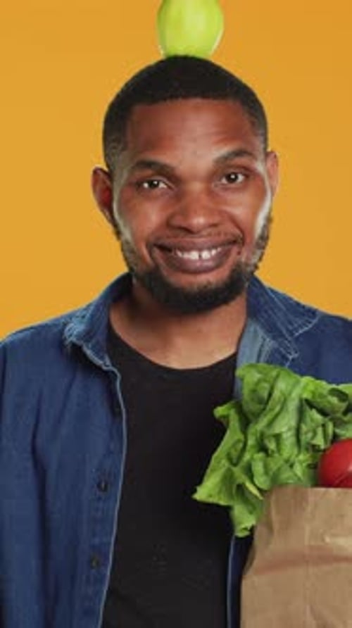 Vertical Video Young Adult Trying to Keep Balance with an Apple on His Head in Studio