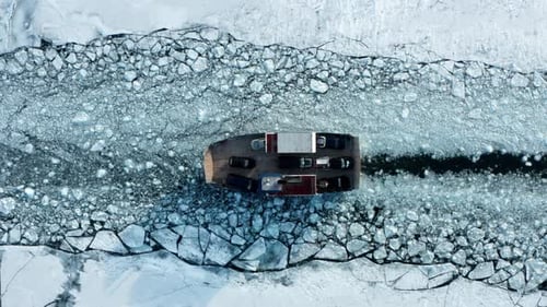 Car ferry transporting vehicles through broken frozen lake ice sheet path, aerial top down