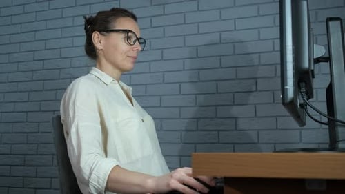 Woman Removing Glasses at Computer Desk