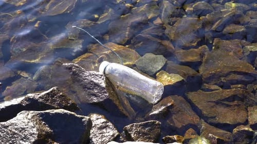 Plastic bottle floating in shallow water of rocky Norway fjord coastline.