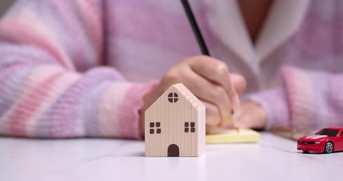 Person Writes Near a Miniature House and Car