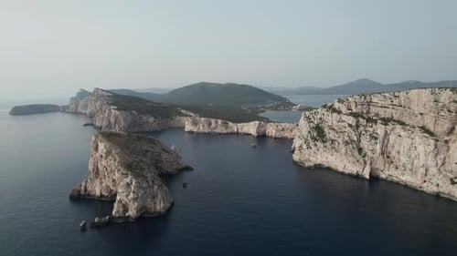 Aerial orbiting view of a sea cliff in a blue ocean at sunset. Sea waves on beautiful landscape aeri