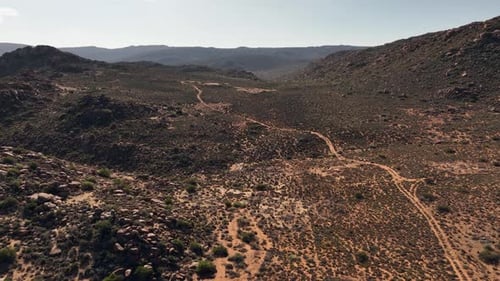 Flyover rugged red sandy desert terrain, rough two-track road below
