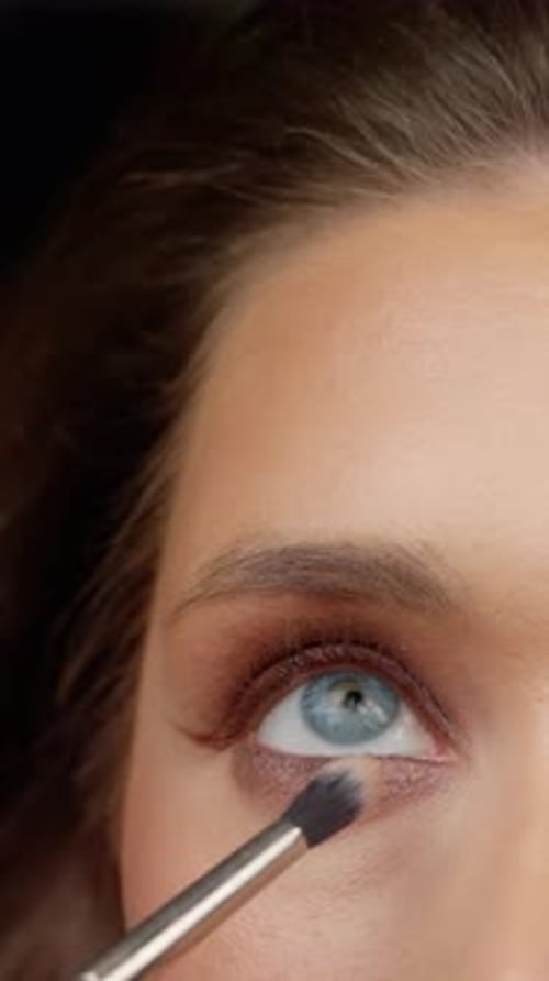 Erfahrener Make-up-Profi, der mit einem Präzisionspinsel vorsichtig lebendigen Lidschatten aufträgt