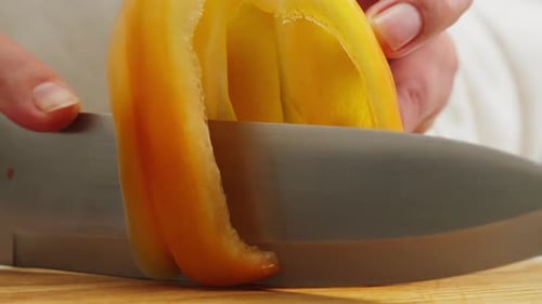 Couper du poivron jaune doux sur un bureau en bois avec un couteau, gros plan, macro, légumes coupés à la main, nourriture