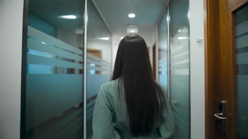 Thoughtful businesswoman walking through modern office hallway alone