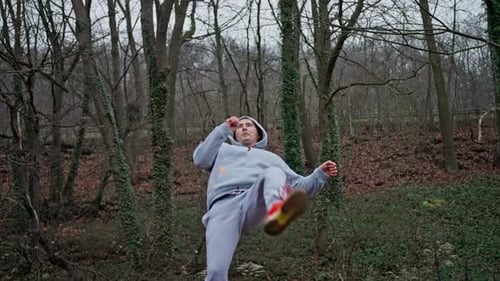 Man in sweats practicing kicks in the woods
