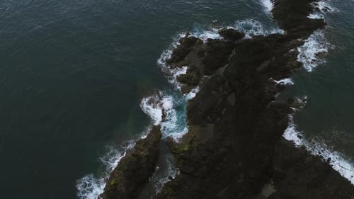 Top Down Aerial View Of Dark Ocean Waves Swirling Rocks