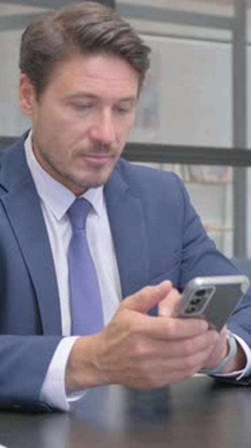 Professional Man Concentrating While Using Cell Phone at Desk