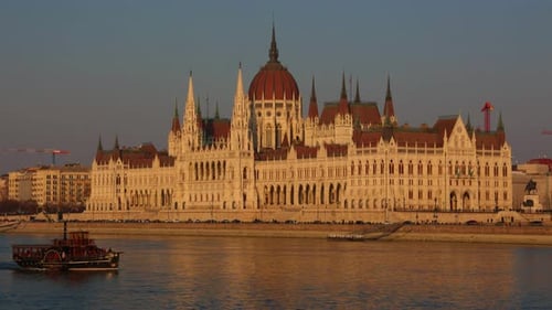 Hungarian Parliament Building with tourist boat sailing on Danube river at sunset