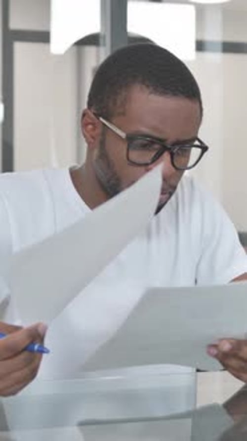 Young Adult Man Reviews Documents with Pen in Office