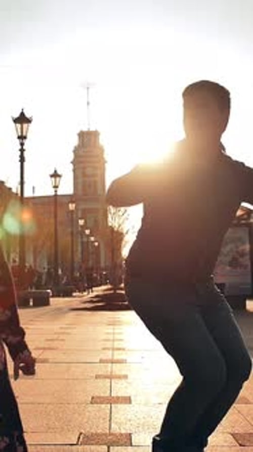 Vertical of Playful Happy Young Couple Male and Female is Jumping Down the Street and Laughing