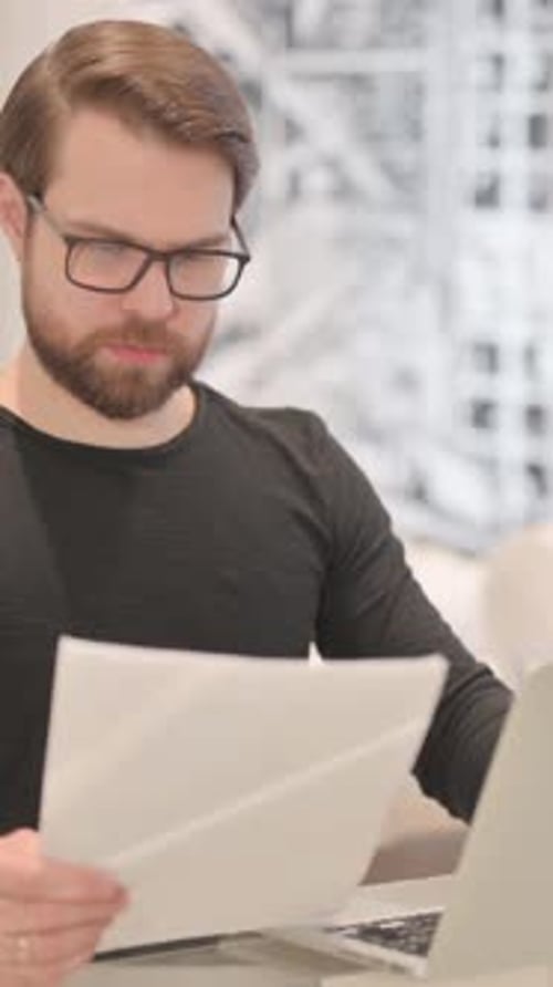 Man Reviews Documents at Desk with Laptop