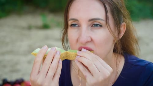Femme mangeant du melon avec une expression concentrée et un comportement détendu, femme mordant une tranche de melon tout en