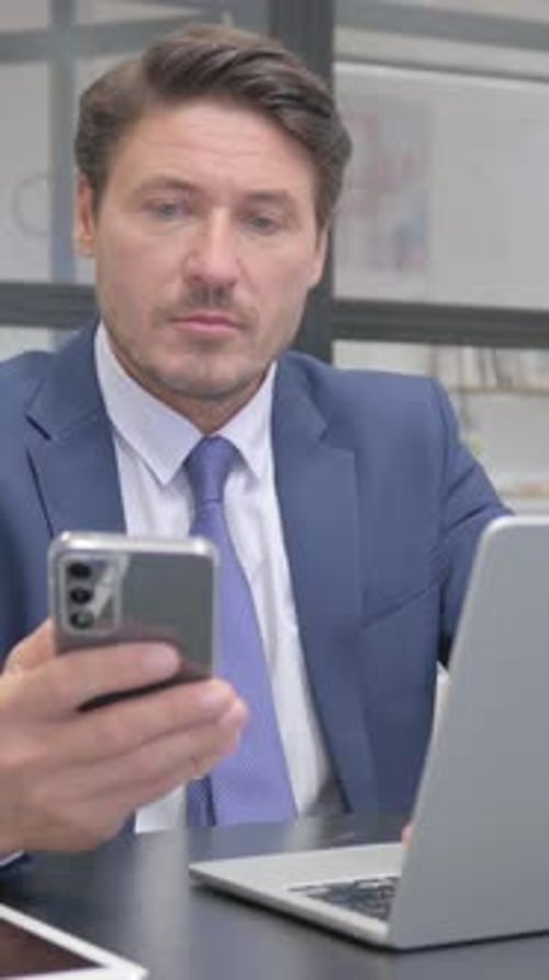 Man in Suit Using Phone and Laptop at Desk