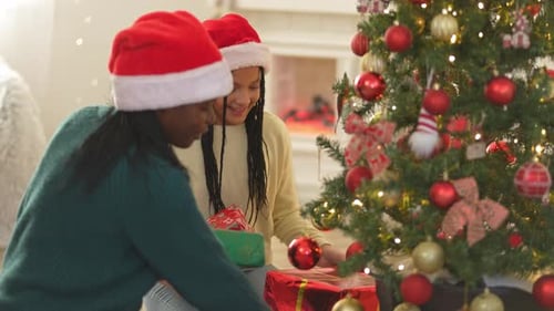 Multiethnic sisters in Santa hats putting presents under a decorated Christmas tree