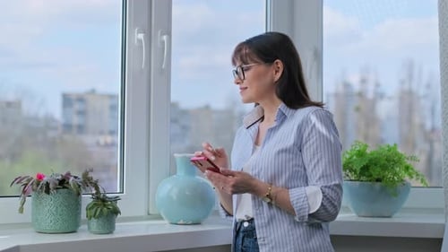 Woman Using Cell Phone By Window At Home