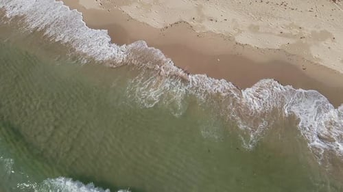 Aerial shot of clear ocean small waves crashing on a white sand beach