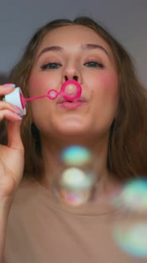 Happy Portrait of Young Smiling Woman Blowing Soap Bubbles and Looking at Camera
