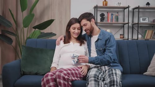 Loving couple sitting with baby shoes on couch