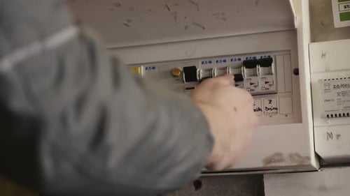 Caucasian hand switching on and of fuses in box on the wall. Close up shot.