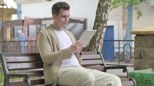 Man Using Tablet on a Bench Outdoors