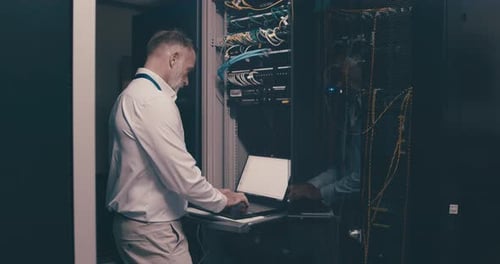 Mature man in data center with laptop, software for network maintenance