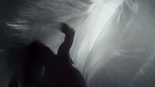 Silhouetted Dancer Performing Gracefully between Flowing Plastic Curtains