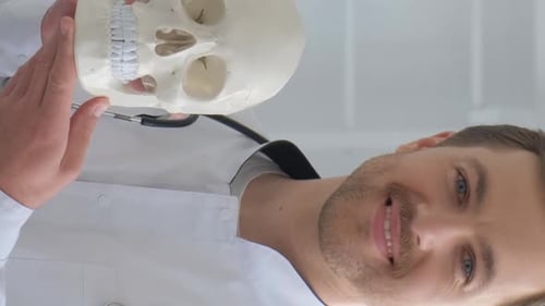 Der Doktor hält einen menschlichen Schädel in seinen Händen und lächelt in die Kamera Vertikales Video