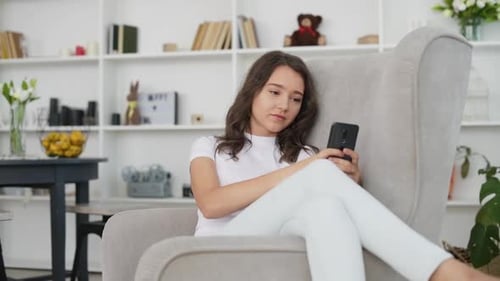 Young Woman Relaxing in Armchair Using Smartphone
