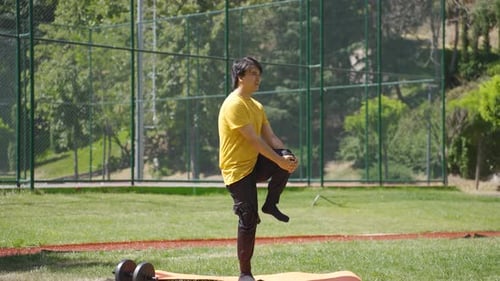 Young man exercising in the park is working out his legs and abs.