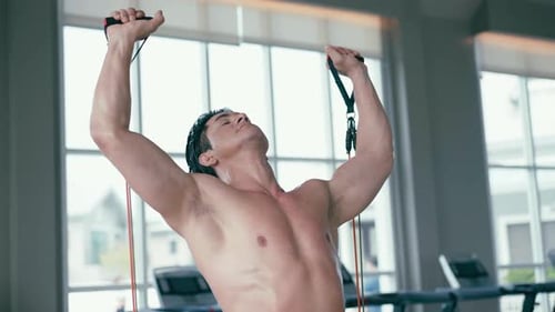A muscular man pulling an exercise resistance band in a gym
