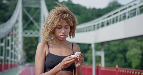 Young African American Woman Putting on Earphones Before Jogging Outdoors on City Bridge