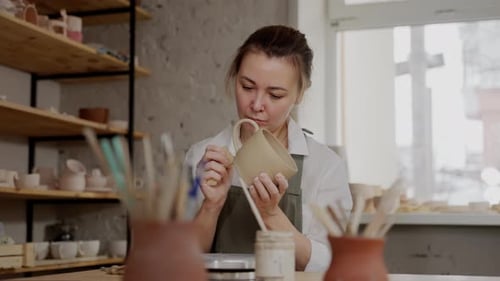 A Woman is Painting a Ceramic Mug in a Pottery Studio