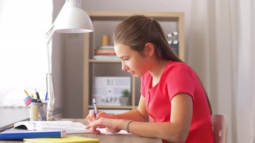 Teen Girl Studying at Desk Indoors Under Lamp