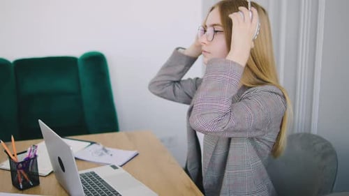 Woman Puts On Headphones at a Desk