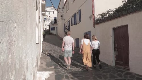 Slow motion, three friend tourists walking up narrow European alleyway in Spain